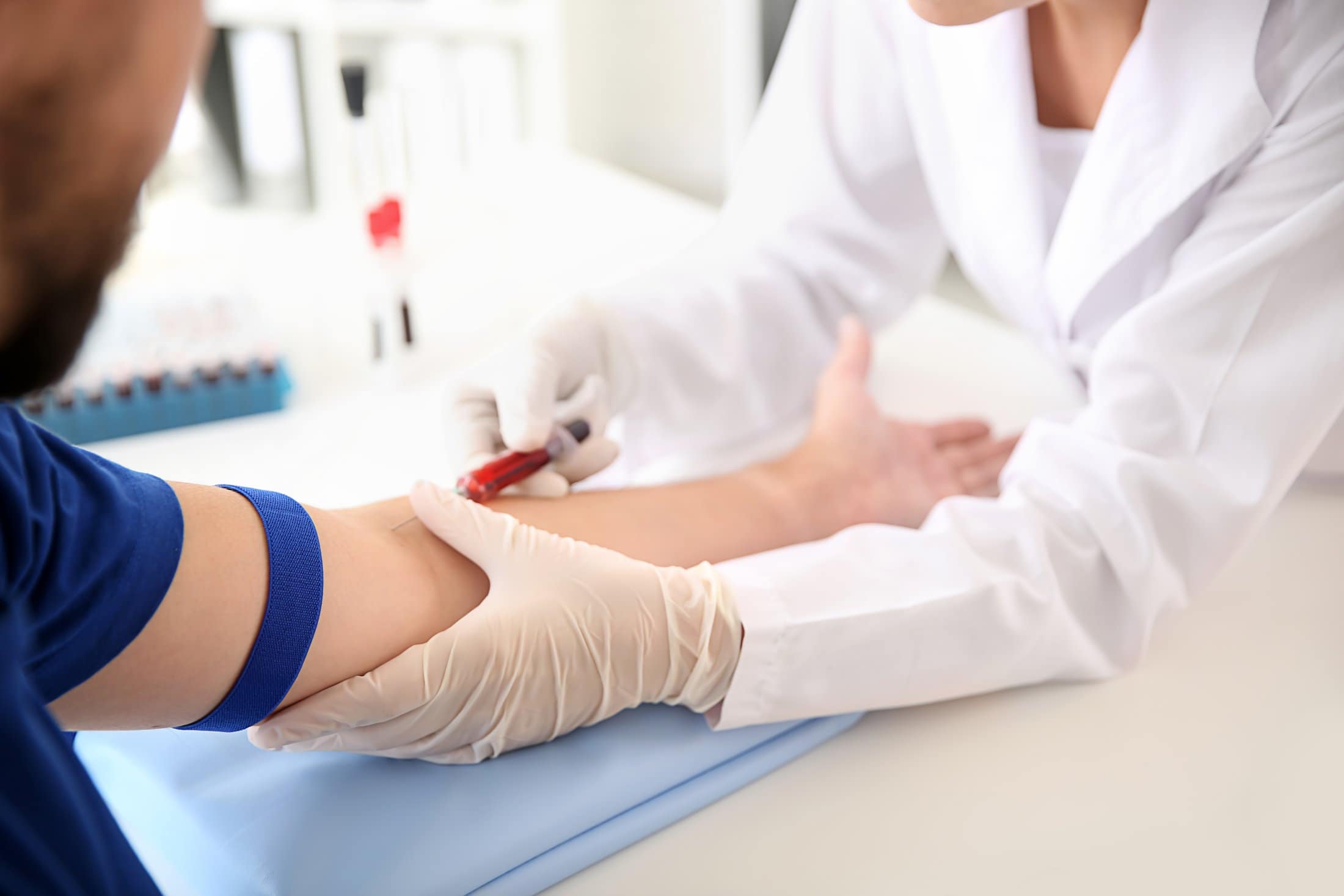 A nurse in gloves drawing blood from a patient's arm