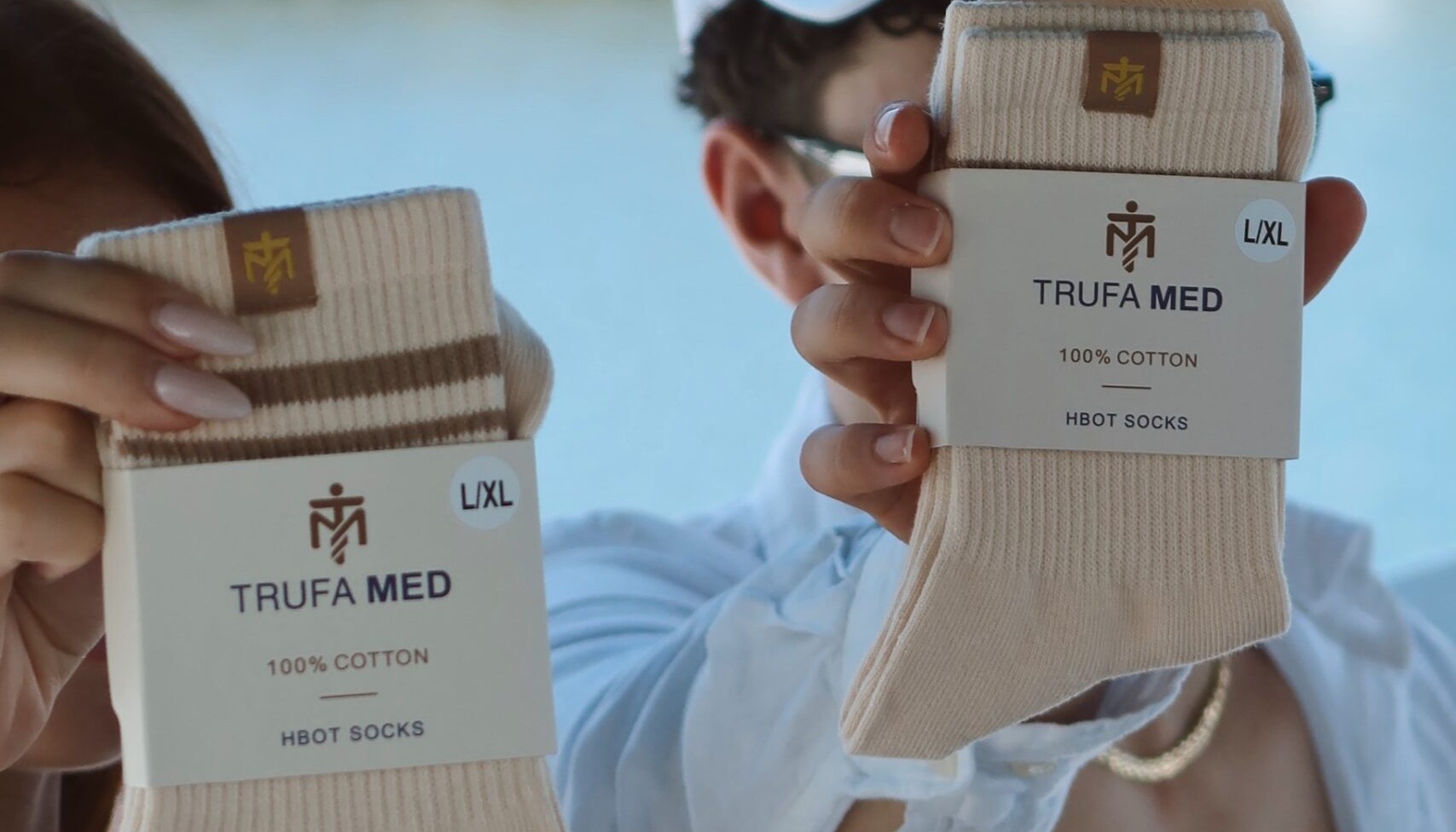Hand holding TrufaMED HBOT socks in retail packaging labeled 100% cotton, Miami waterway behind